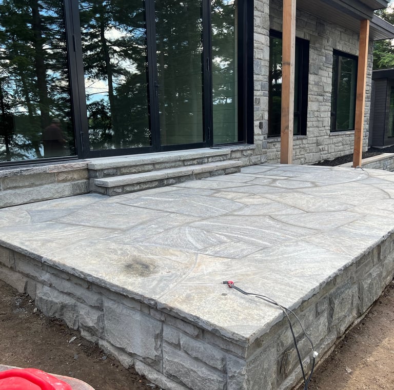 Custom granite flagstone patio and stone steps outside a modern luxury lake house.