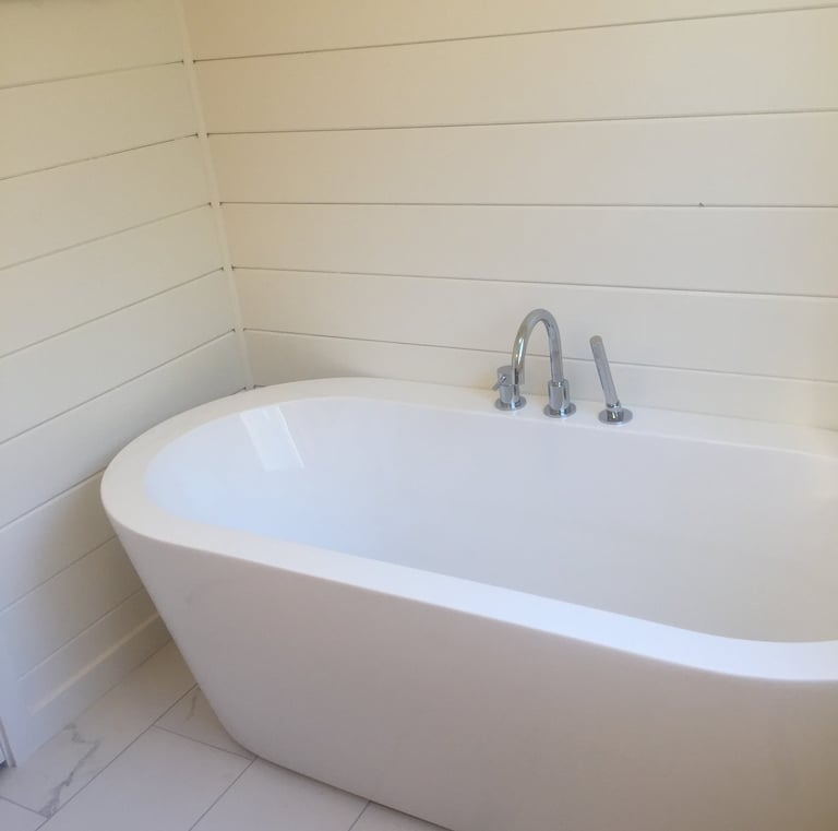 Modern white freestanding soaking bathtub with chrome faucet against cream shiplap walls.