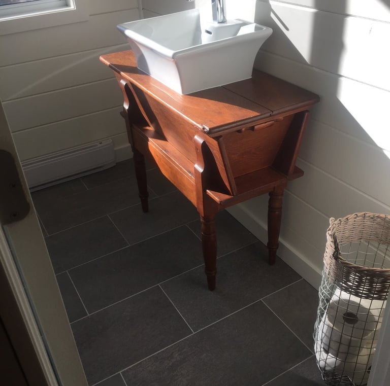White vessel sink on a vintage wood vanity in a bathroom with dark grey floor tiles.