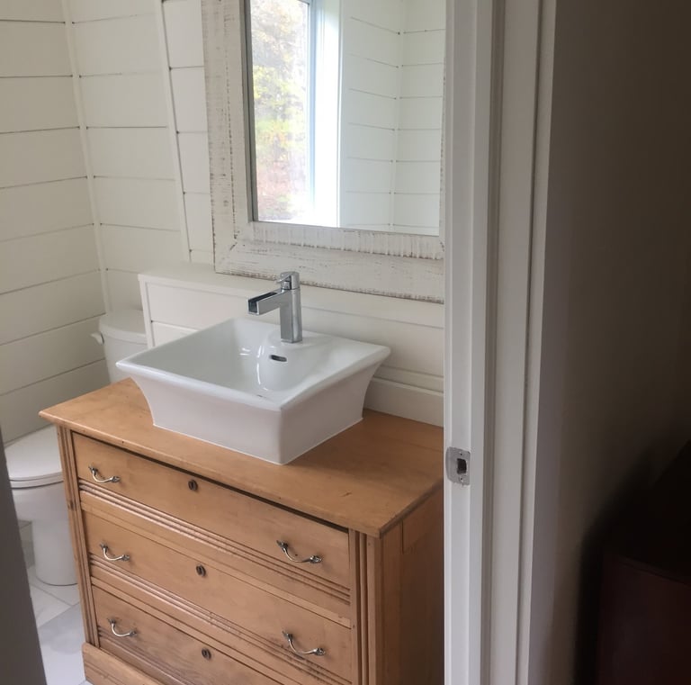 Rustic bathroom vanity featuring a wooden dresser with a white vessel sink and shiplap walls.