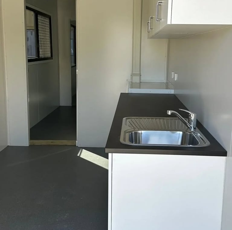 A modern kitchenette inside a portable site office cabin featuring a stainless steel sink and dark countertop.