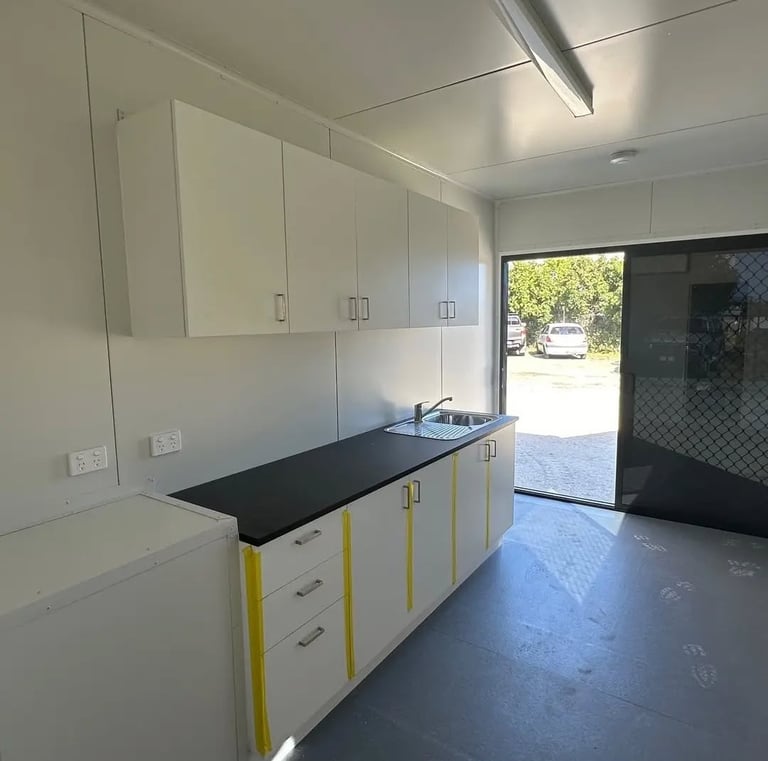 Modern portable cabin kitchenette featuring white cabinets, black countertop, and stainless steel sink.