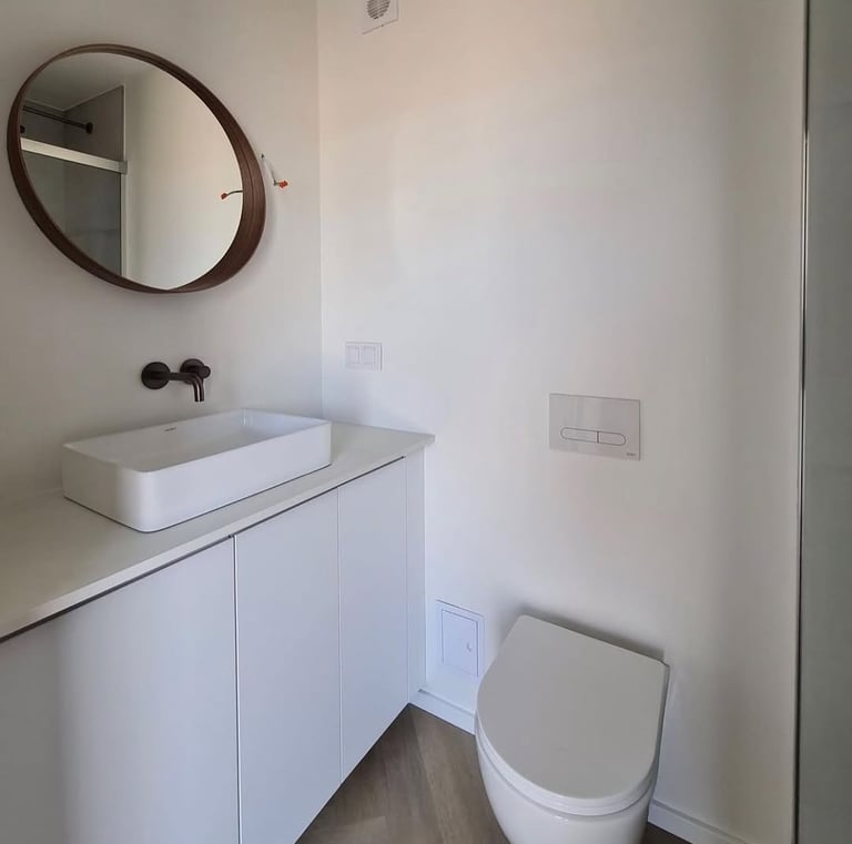 Modern minimalist bathroom with a white vessel sink, floating vanity, round mirror, and wall-hung toilet.