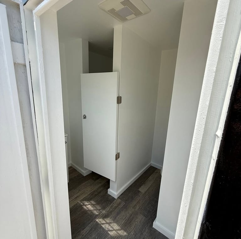 White interior restroom stall with wood-style flooring and modern door hardware.