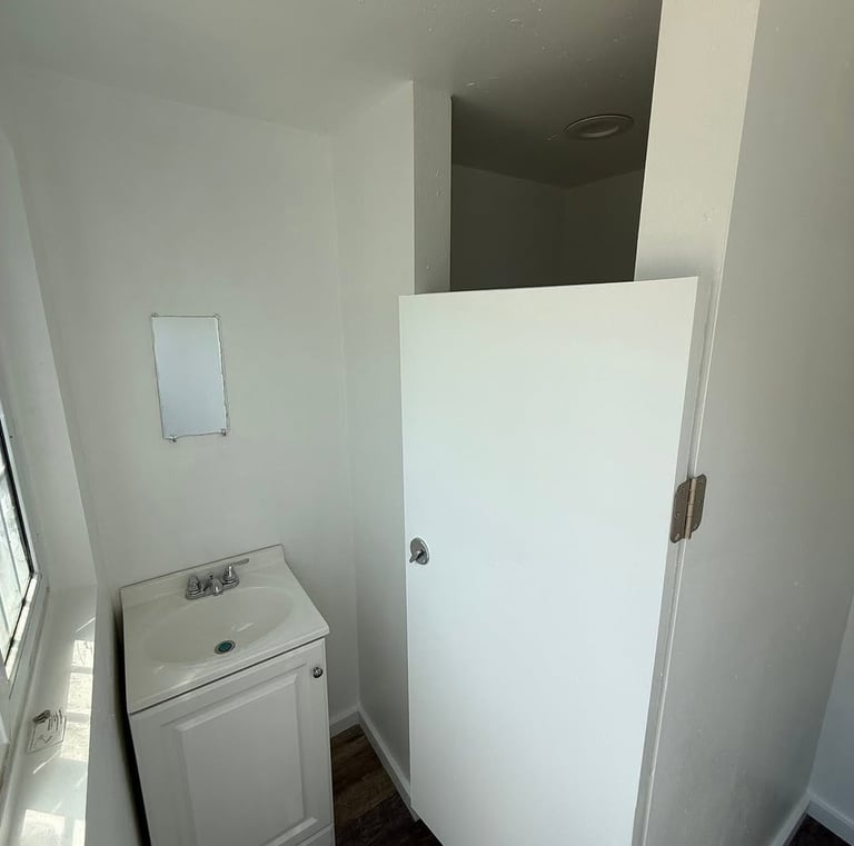 Small white bathroom vanity with a ceramic sink next to a white privacy partition door.