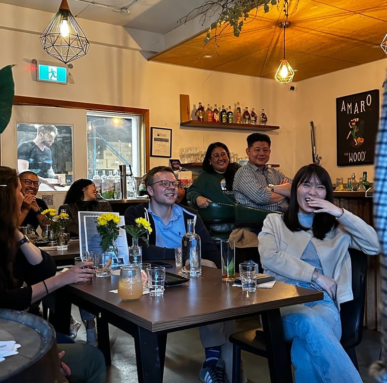 A diverse group of friends laughing and enjoying drinks at a cozy bar with industrial pendant lighting.