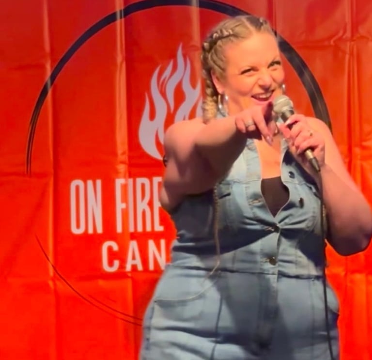 Female stand-up comedian performing on stage with a microphone in front of an On Fire comedy backdrop.