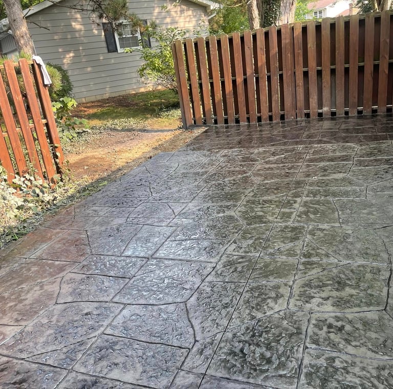 Custom decorative stamped concrete patio with slate texture and brown wooden privacy fence.