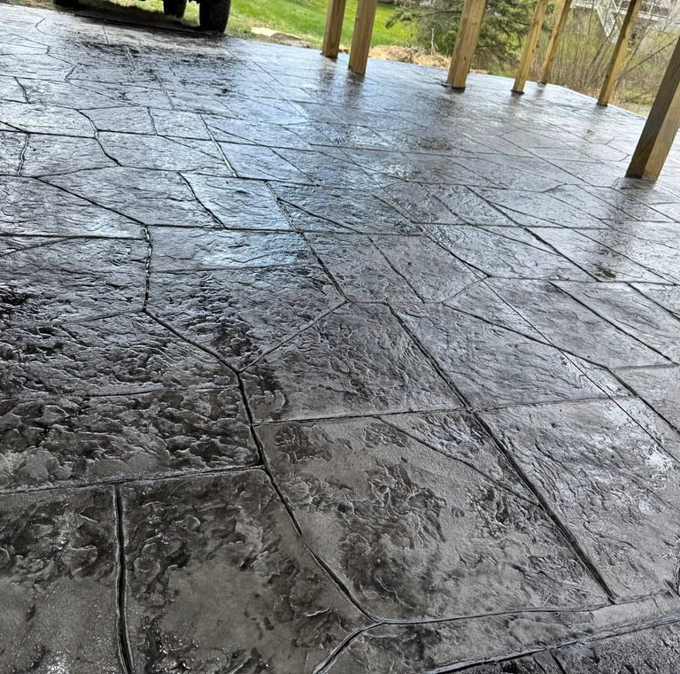 Dark gray stamped concrete patio with a glossy wet-look sealer and flagstone pattern.
