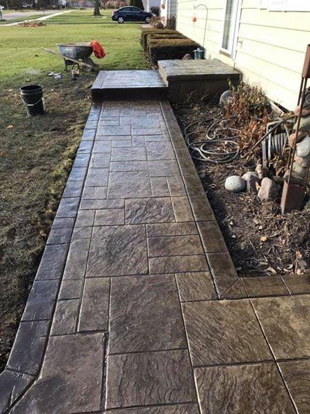 Custom dark brown stamped concrete walkway with a slate pattern leading to a home entrance.