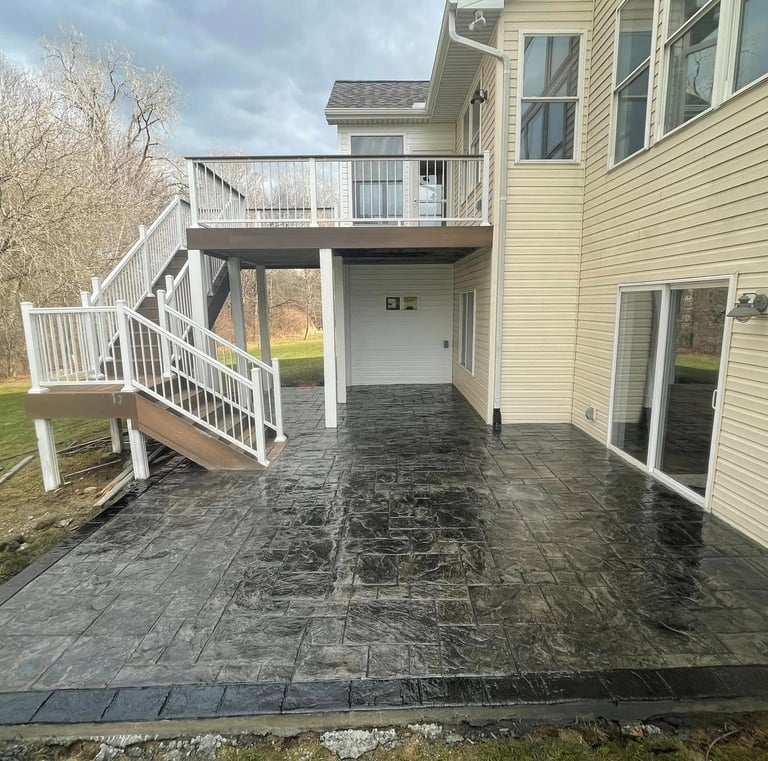 New dark grey stamped concrete patio installed under a two-story residential deck with white railings.