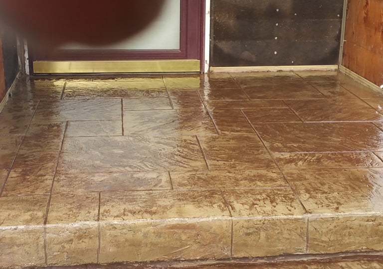 Custom brown stamped concrete patio entryway with a gloss finish and textured stone pattern.