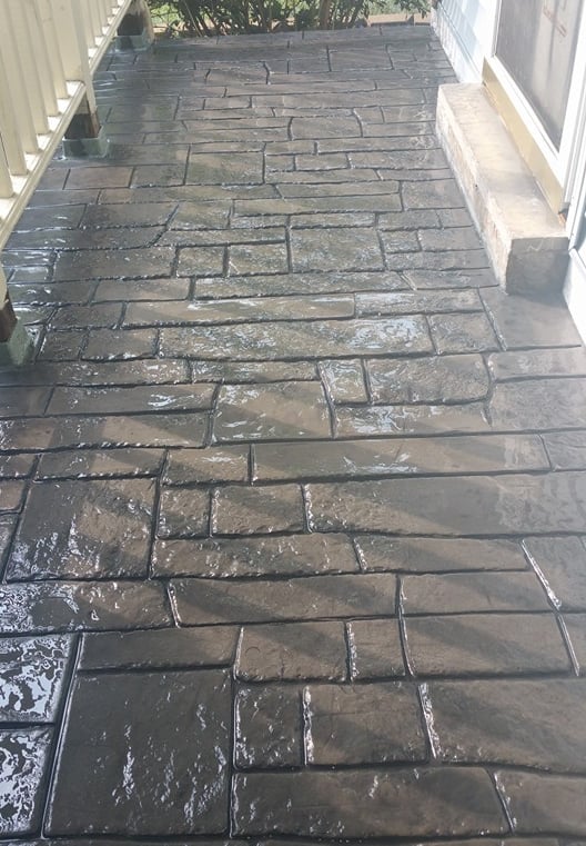 Freshly sealed grey stamped concrete patio with a decorative flagstone pattern and glossy finish.