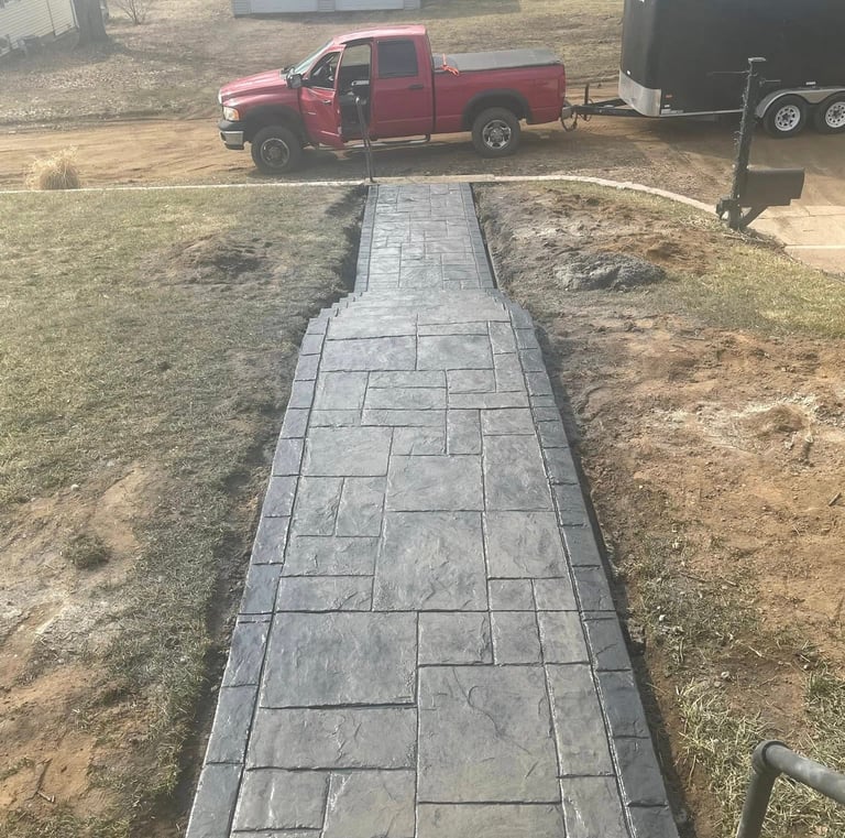Custom stamped concrete walkway with a dark grey ashlar slate pattern leading to a residential driveway.