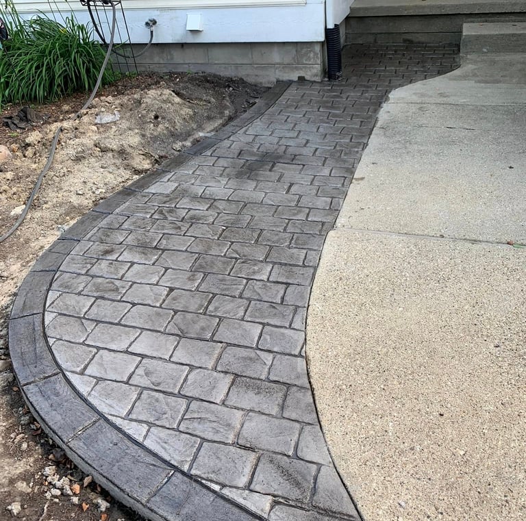 Curved grey stamped concrete walkway with a brick pattern leading to a residential front porch.