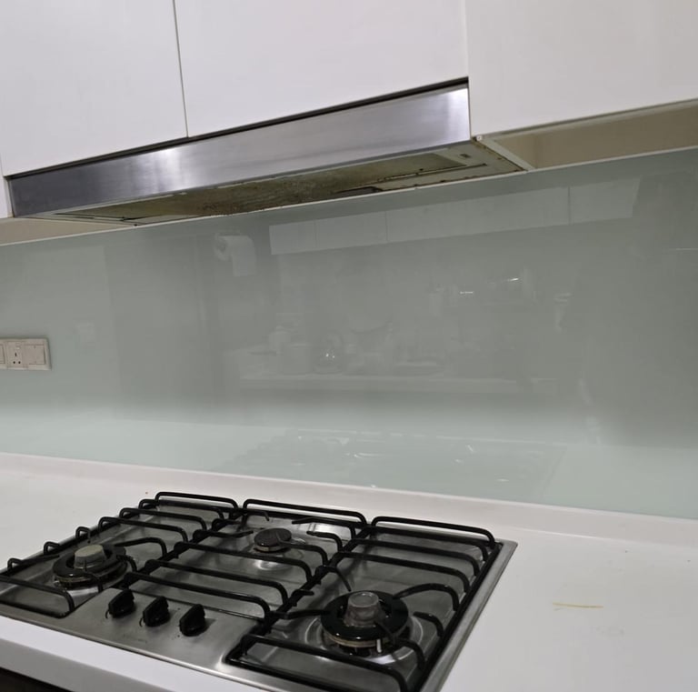 Modern kitchen featuring a sleek glass backsplash behind a stainless steel gas stove and range hood.