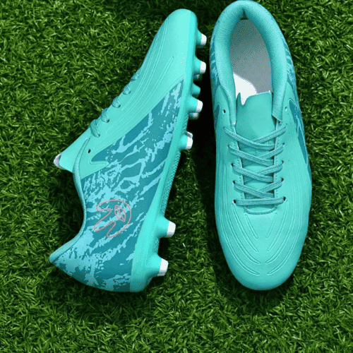 Un par de botas de fútbol de color azul turquesa sobre un campo de césped artificial verde.