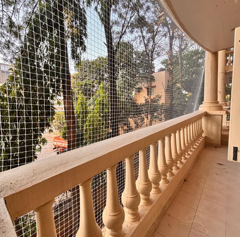 Sunlight filtering through a white balcony safety net against the Mumbai skyline.