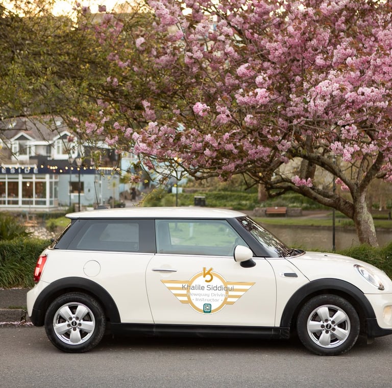 White Mini Cooper driving instructor car parked by pink cherry blossom trees in Newquay.