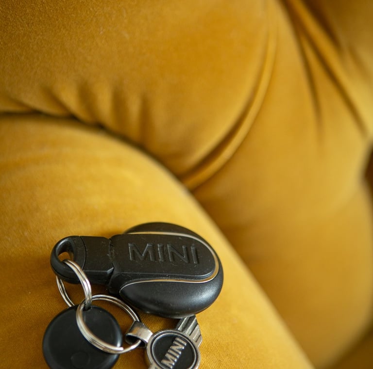Black Mini Cooper car key fob and silver logo keychain resting on a yellow velvet couch.