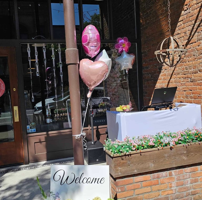 A DJ setup in front of a bridal shop with flowers, balloons and a welcome sign