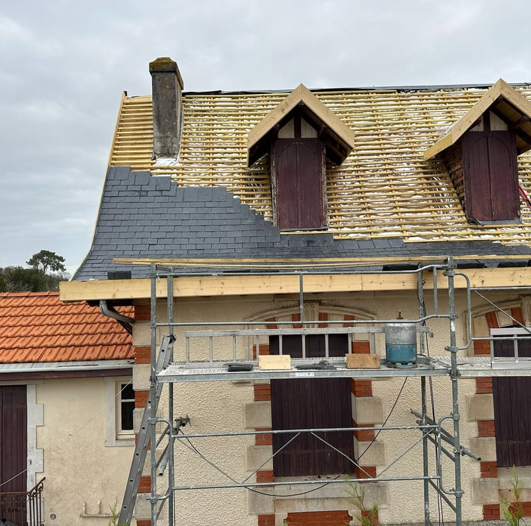 Installation professionnelle de toiture en ardoise sur une maison avec échafaudage et lucarnes.