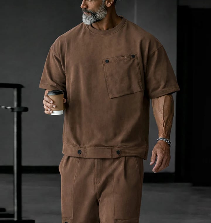 Athletic man wearing a brown oversized t-shirt and matching shorts set while holding coffee.