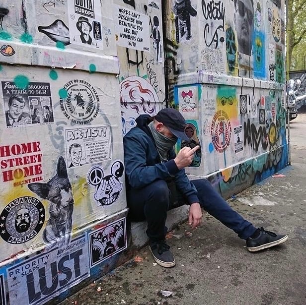 Dacarter in a mask and cap sitting against a wall in Star Yard Brick Lane