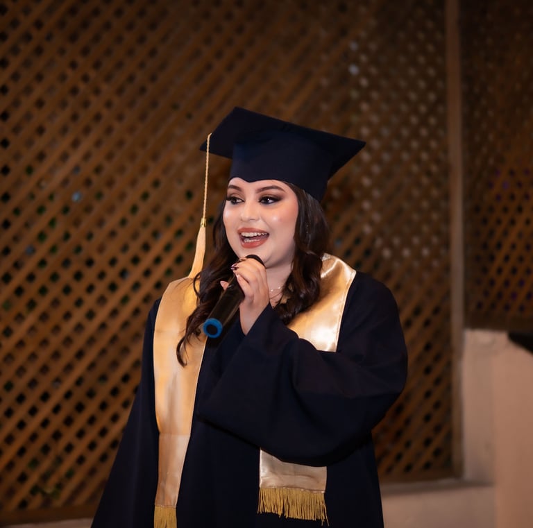 Una mujer graduada sonriente con toga y birrete negros da un discurso frente a un micrófono.