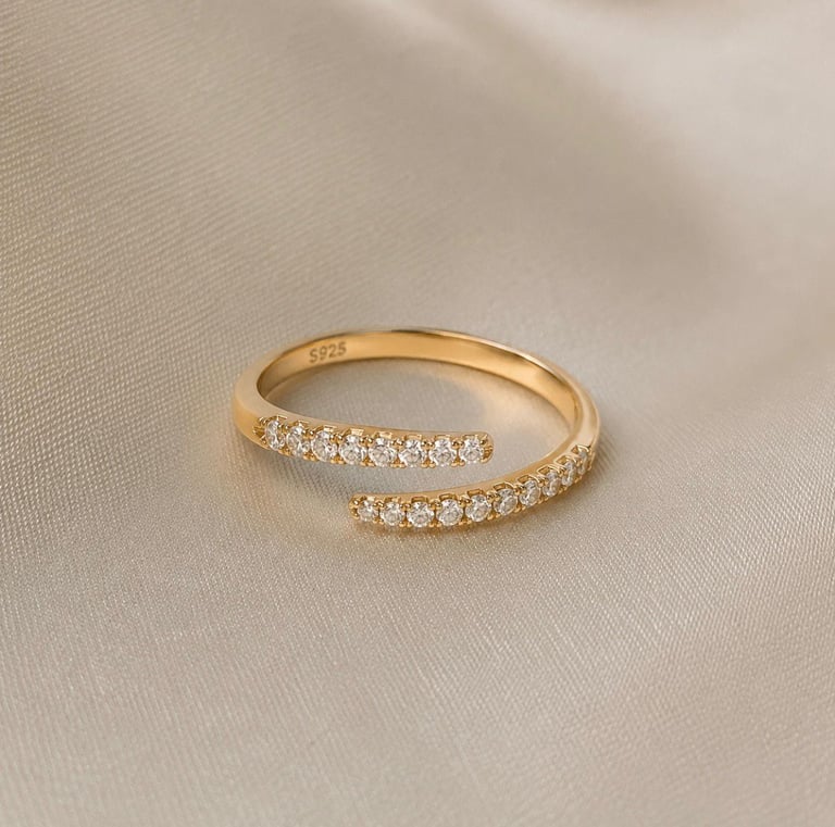 Minimalist gold crystal open ring displayed on a soft cream fabric background.