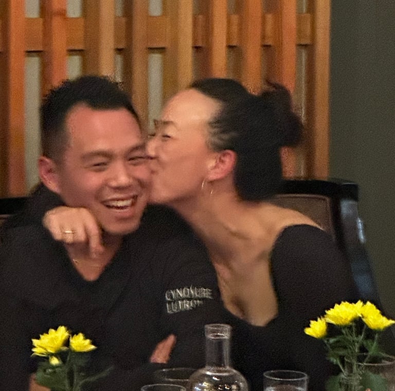 A happy couple sharing a kiss at a dinner table with yellow flowers and wooden decor.