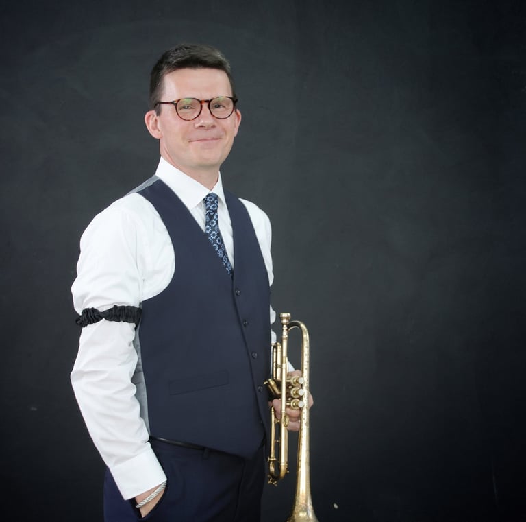 George Chase wearing a vest, tie and arm garters, holding a cornet.