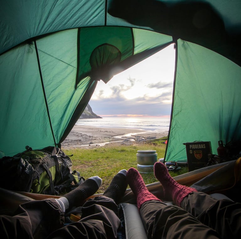 people laying in a tent camping with their feet up next to the sea