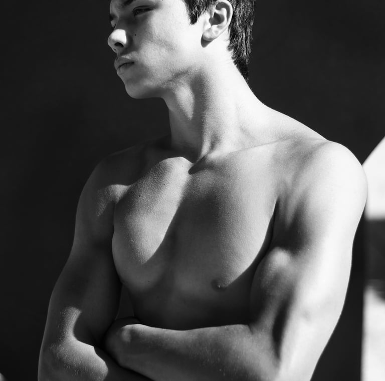 a young muscular man standing looking aloof with folded arms