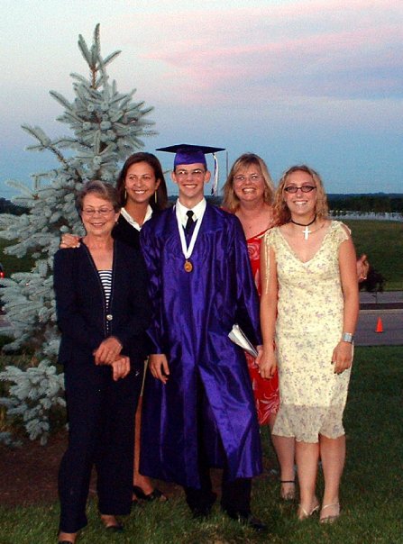 A high school graduate in a purple cap and gown poses with family outdoors at sunset. Athens, Oh