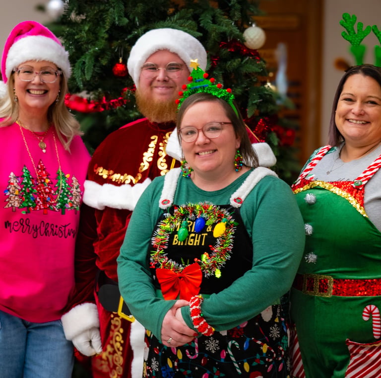Four people wearing festive Christmas outfits and Santa hats posing in front of a X-mas tree. Athens