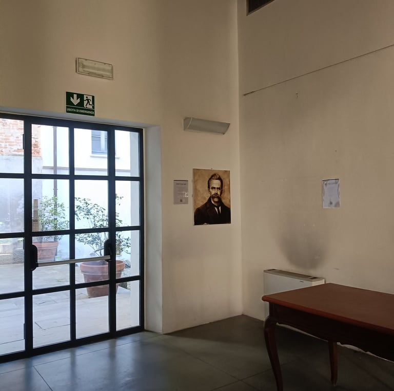 Nietzche a glass door, a wooden desk, and a portrait hanging on a white wall.