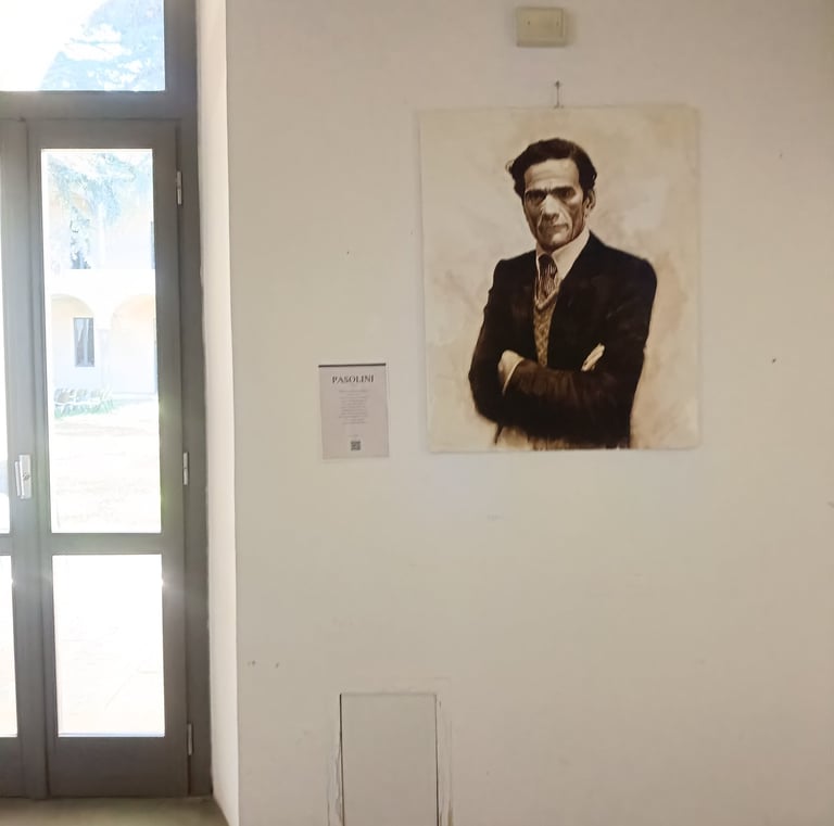 Portrait painting of Pier Paolo Pasolini displayed on a white art gallery wall next to a glass door.