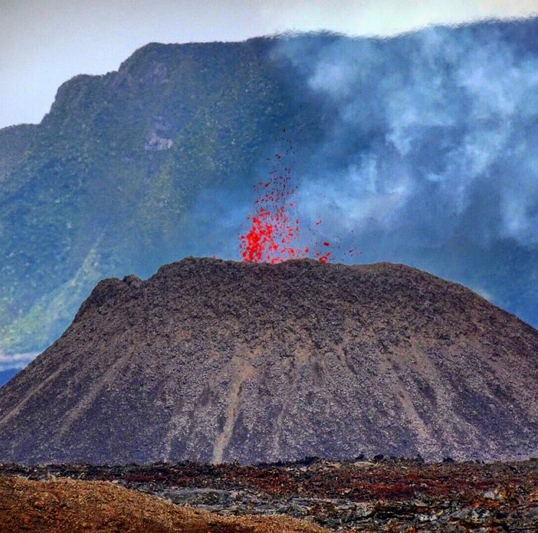 Red hot lava erupting from a volcanic cinder cone crater with smoke and mountain landscape.