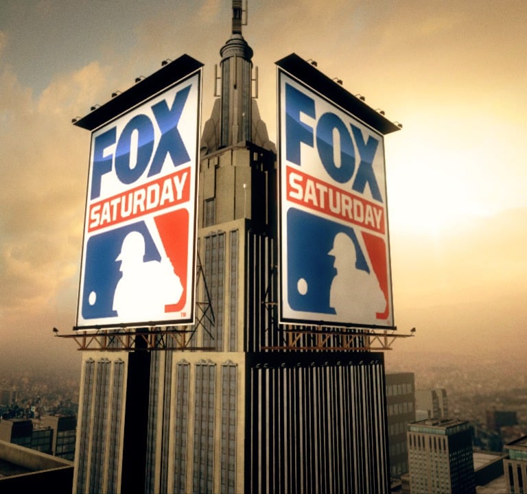 MLB Fox Saturday banners hang on a skyscraper with a sunset cityscape in the background