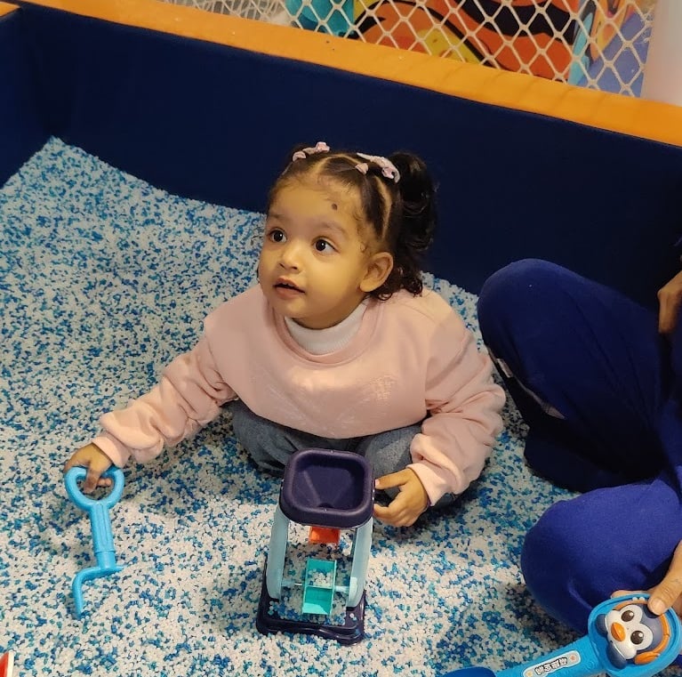a baby girl sitting on a bed with a toy truck