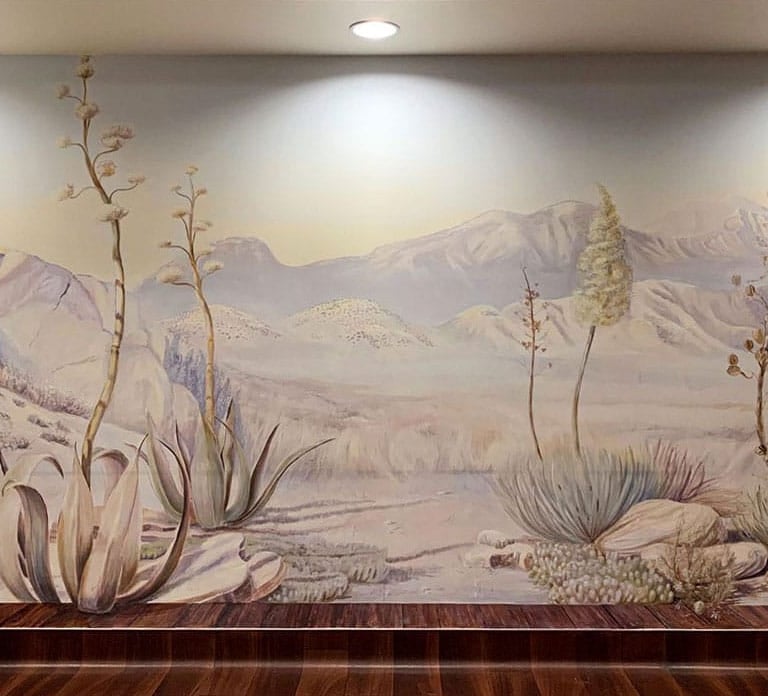 Full view on a desert mural, painted in soft beige, green and lilac colours, overlooking mountains, boulders and desert plant