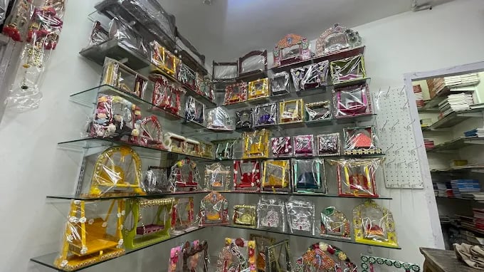 A collection of colorful decorative wooden swings for Hindu idols displayed on glass shelves in a shop.