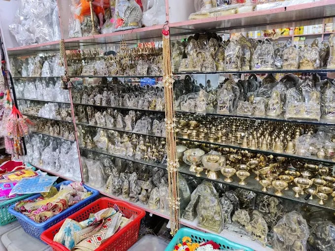 Brass and silver plated Hindu deity idols and puja items displayed on glass shelves in a shop.
