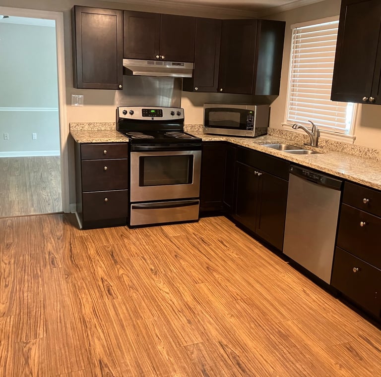 Modern kitchen with dark wood cabinets, granite countertops, and stainless steel appliances over hardwood floors.