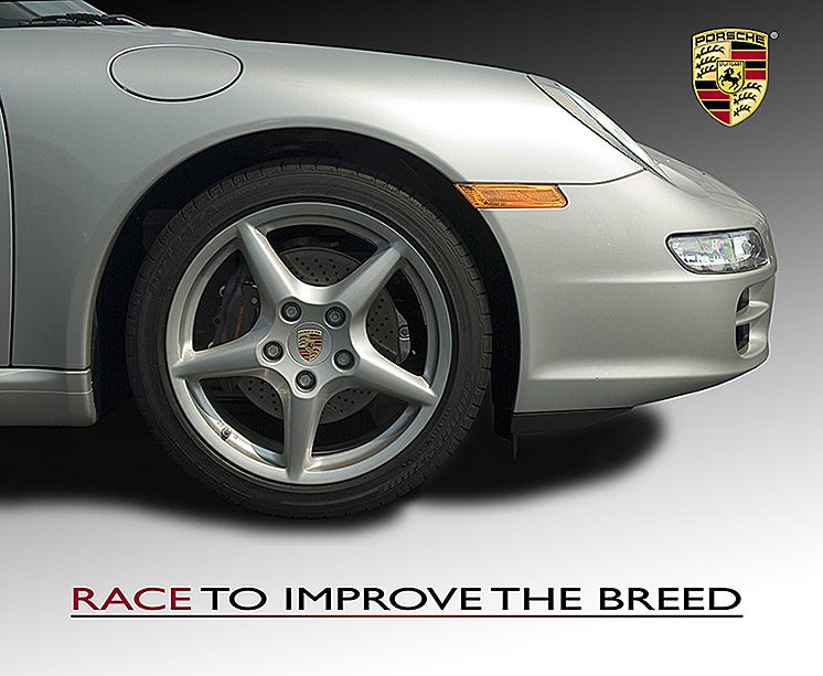 Close-up of a silver Porsche 911 front wheel and alloy rim with the brand logo and race slogan.