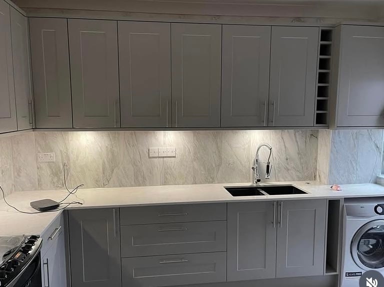 Modern grey shaker kitchen cabinets with marble backsplash and under-cabinet lighting.