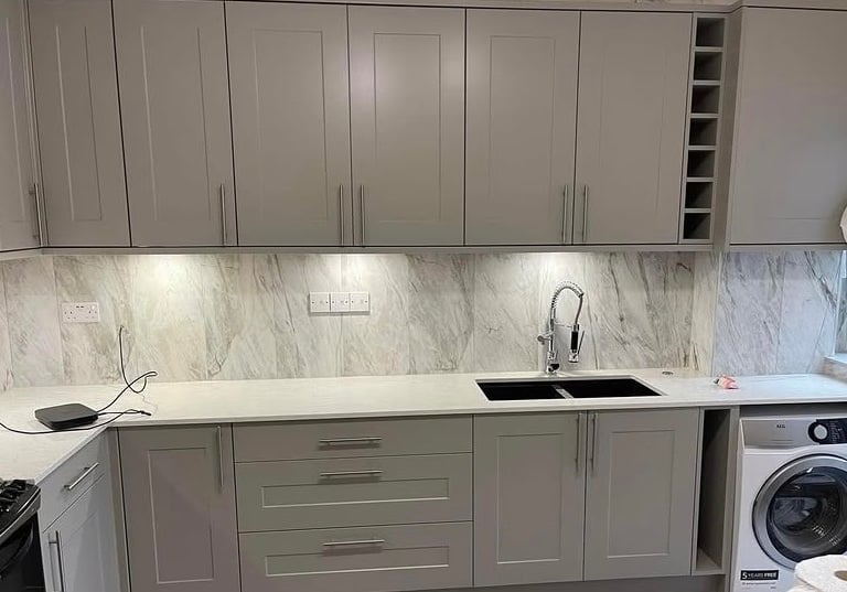 Modern grey kitchen cabinets with marble backsplash, white countertops, and integrated appliances. 