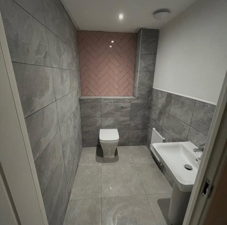Modern bathroom featuring grey stone tiles and a pink herringbone accent wall.