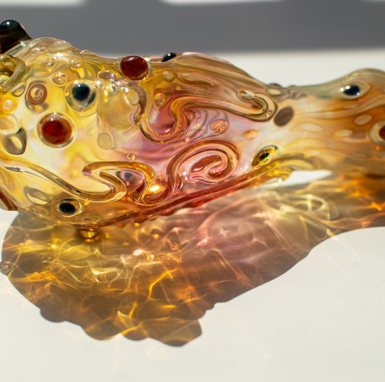 Handblown glass spoon pipe with intricate amber fumed patterns and colorful glass dots for smoking.